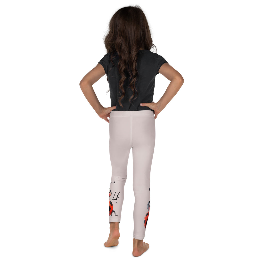 Lovebugs Girls Leggings, sand-colored background with a female ladybug with big eyes at the bottom of one leg and a male ladybug looking delighted on the other leg, with black swirling lines above them forming hearts on both sides, back view on model