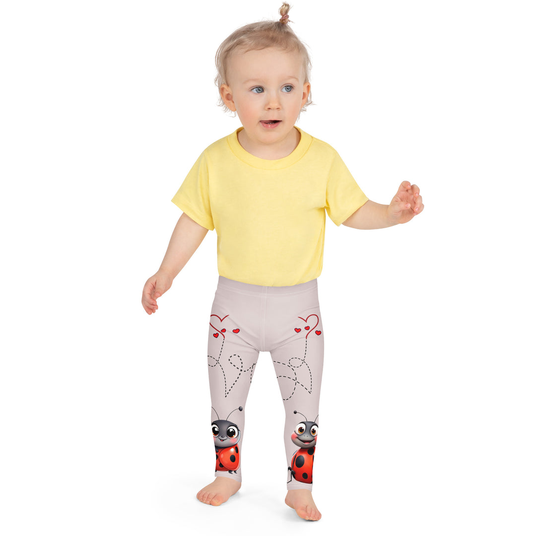 Lovebugs Girls Leggings, sand-colored background with a female ladybug with big eyes at the bottom of one leg and a male ladybug looking delighted on the other leg, with black swirling lines above them forming hearts on both sides, front close-up view on model