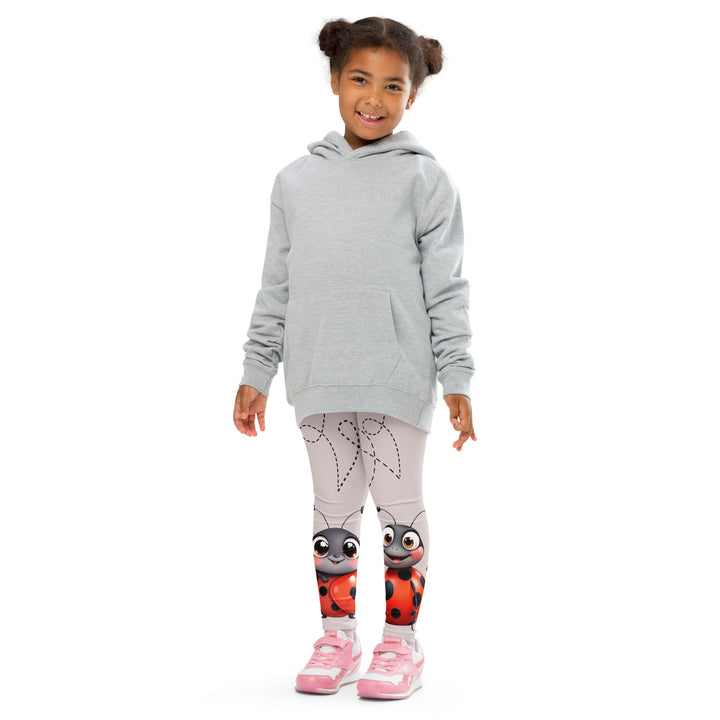 Lovebugs Girls Leggings, sand-colored background with a female ladybug with big eyes at the bottom of one leg and a male ladybug looking delighted on the other leg, with black swirling lines above them forming hearts on both sides, front pose with arms at sides on model