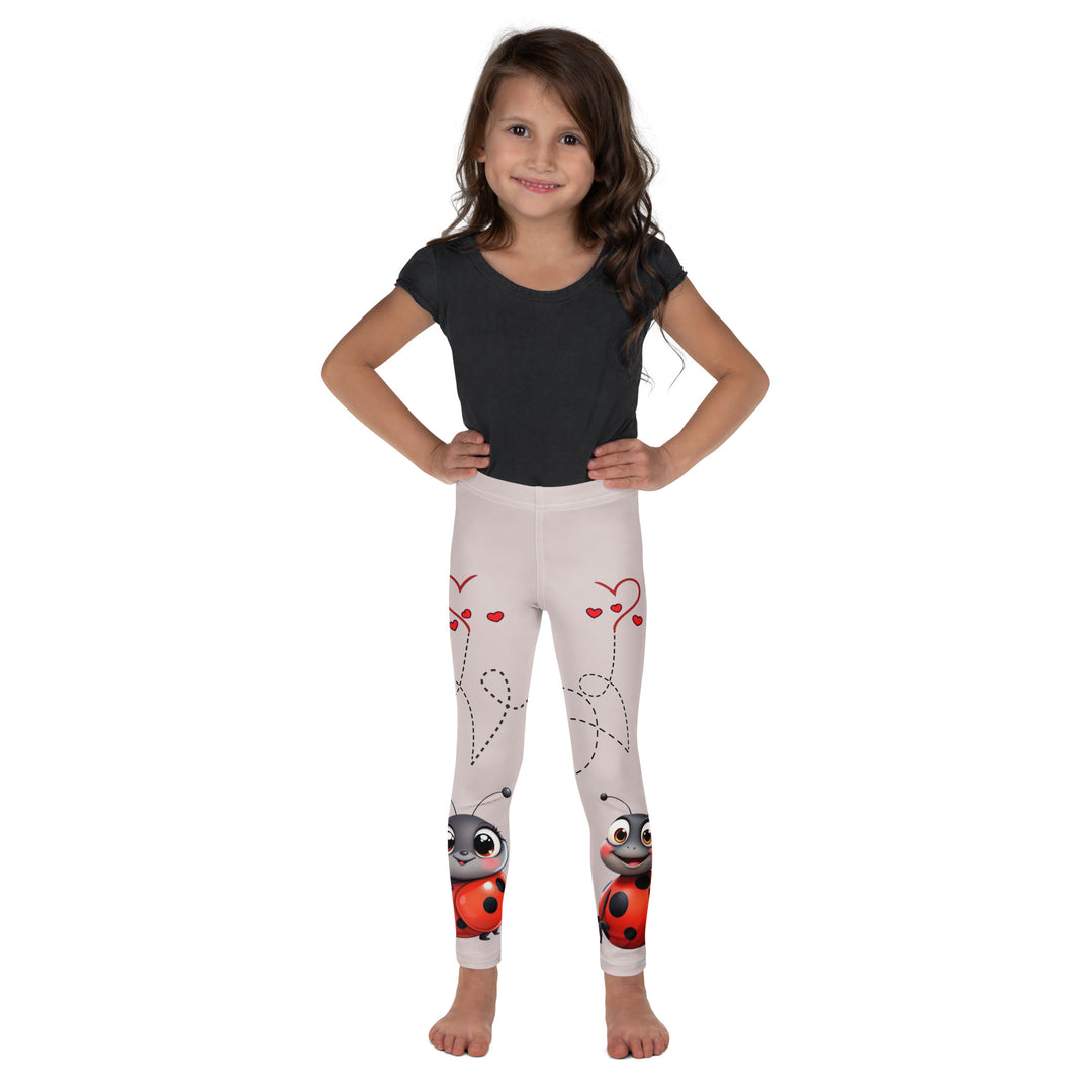 Lovebugs Girls Leggings, sand-colored background with a female ladybug with big eyes at the bottom of one leg and a male ladybug looking delighted on the other leg, with black swirling lines above them forming hearts on both sides, front view on model