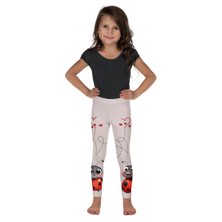 Lovebugs Girls Leggings, sand-colored background with a female ladybug with big eyes at the bottom of one leg and a male ladybug looking delighted on the other leg, with black swirling lines above them forming hearts on both sides, front view on model