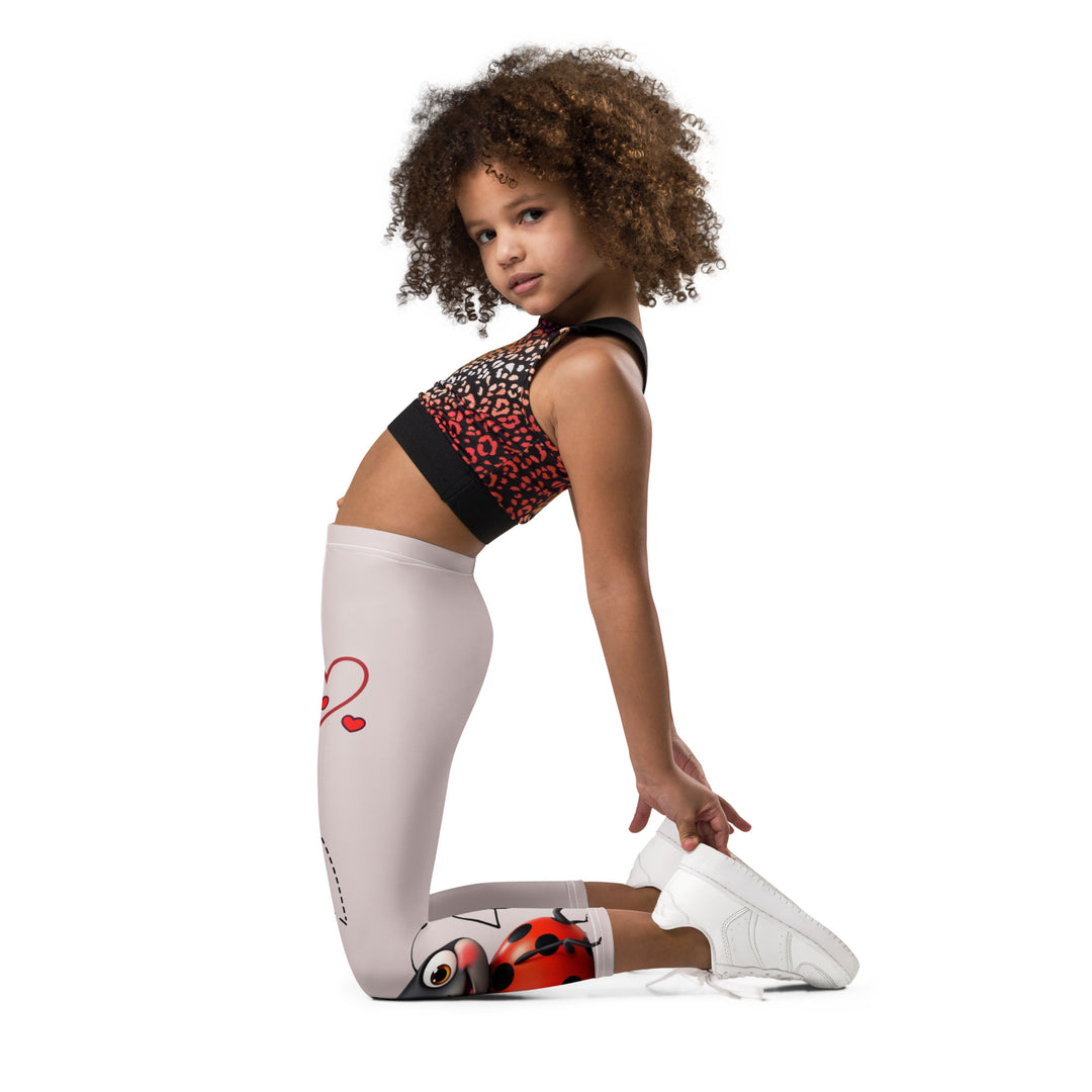 Lovebugs Girls Leggings, sand-colored background with a female ladybug with big eyes at the bottom of one leg and a male ladybug looking delighted on the other leg, with black swirling lines above them forming hearts on both sides, left side view kneeling on model