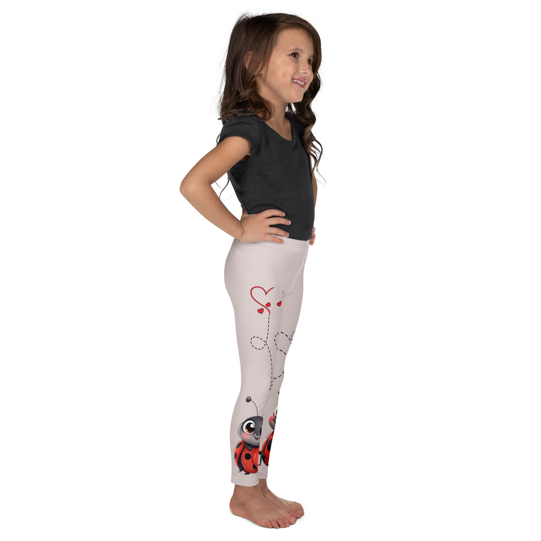 Lovebugs Girls Leggings, sand-colored background with a female ladybug with big eyes at the bottom of one leg and a male ladybug looking delighted on the other leg, with black swirling lines above them forming hearts on both sides, right side view on model