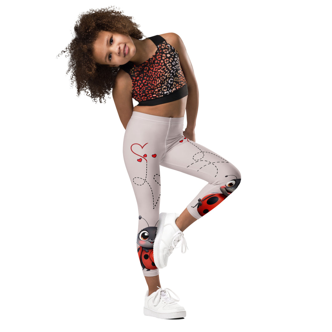 Lovebugs Girls Leggings, sand-colored background with a female ladybug with big eyes at the bottom of one leg and a male ladybug looking delighted on the other leg, with black swirling lines above them forming hearts on both sides, side view with one leg lifted and bent on model