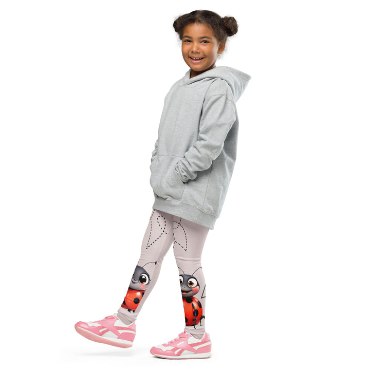 Lovebugs Girls Leggings, sand-colored background with a female ladybug with big eyes at the bottom of one leg and a male ladybug looking delighted on the other leg, with black swirling lines above them forming hearts on both sides, side view with one leg lifted and extended on model