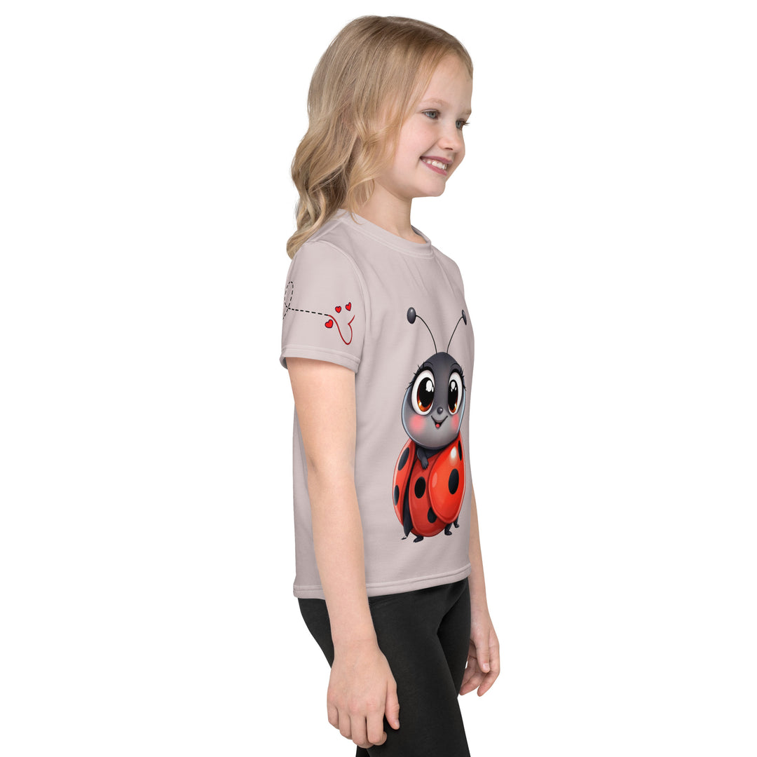 Lovebugs Girls T-shirt, sand-colored background with a smiling female ladybug with big eyes on the front, a happy male ladybug with a heart beside him on the back, and hearts with connecting lines on both sleeves, right side view on model
