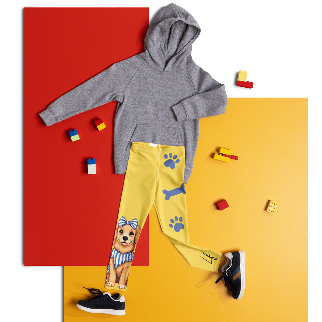 Puppy & Bones Girls Leggings, yellow background with a golden retriever puppy wearing a blue and white striped outfit and a matching blue and white bow on the head on one leg, and blue paw prints and blue bones running down the other leg, front view laid flat on floor