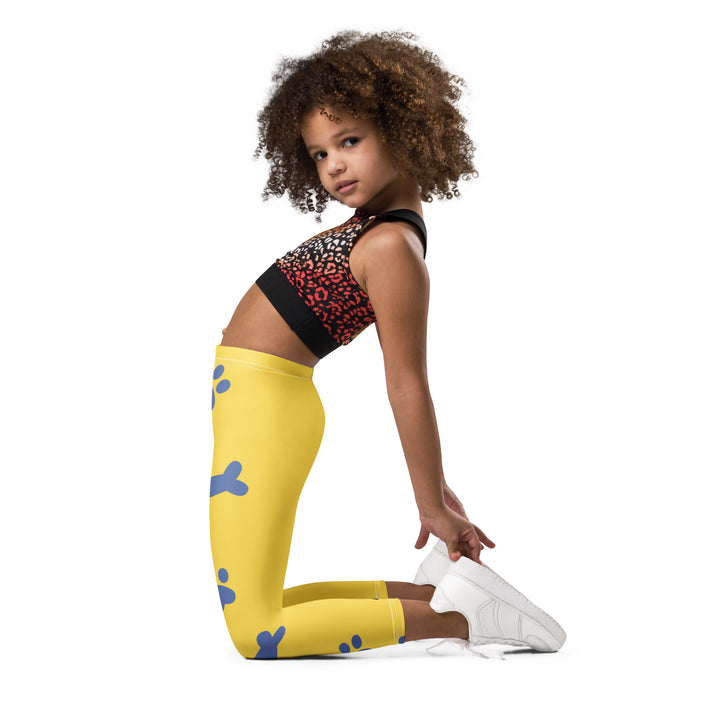  Puppy & Bones Girls Leggings, yellow background with a golden retriever puppy wearing a blue and white striped outfit and a matching blue and white bow on the head on one leg, and blue paw prints and blue bones running down the other leg, left side view kneeling on model