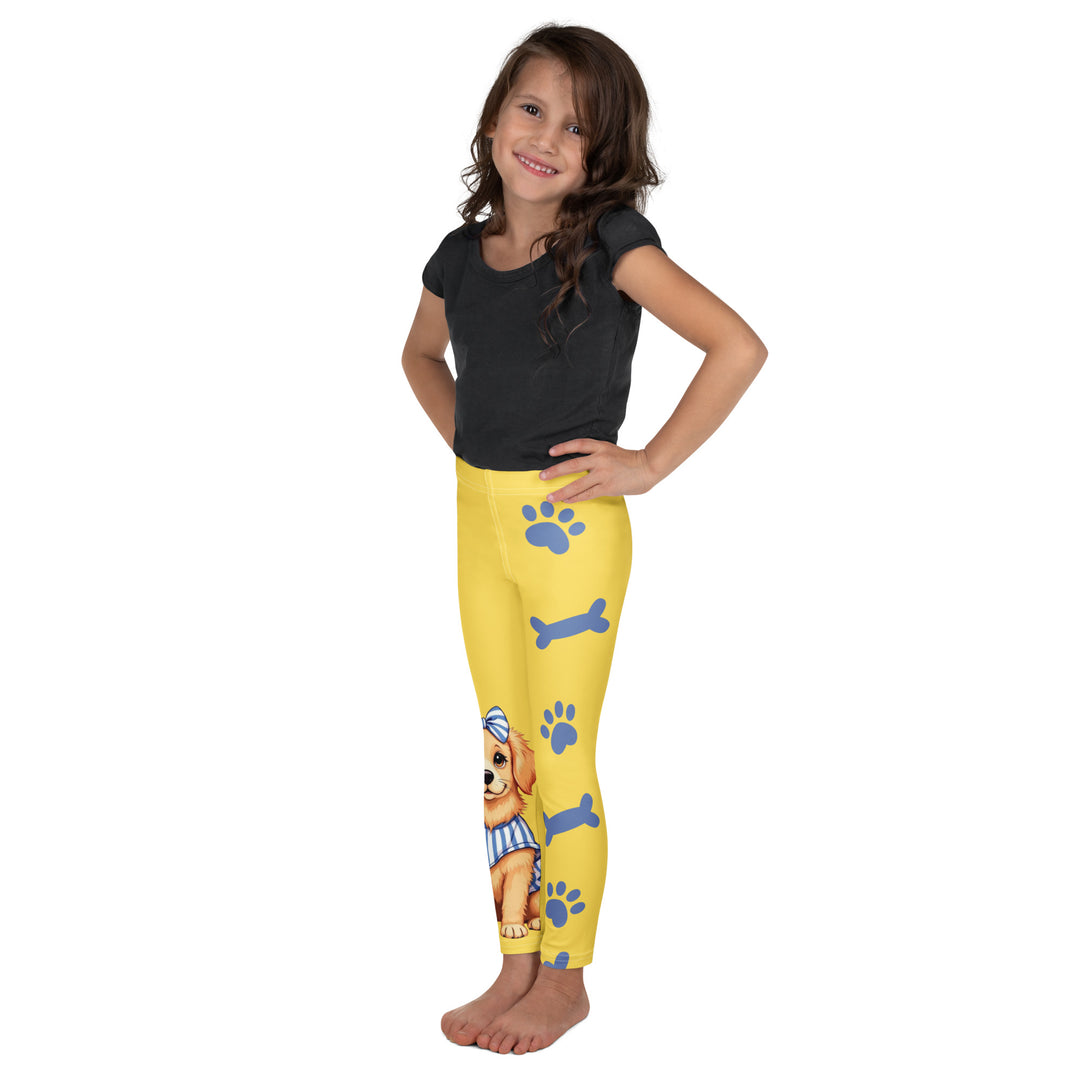 Puppy & Bones Girls Leggings, yellow background with a golden retriever puppy wearing a blue and white striped outfit and a matching blue and white bow on the head on one leg, and blue paw prints and blue bones running down the other leg, left side view on model