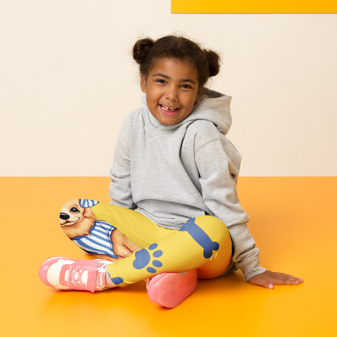 Puppy & Bones Girls Leggings, yellow background with a golden retriever puppy wearing a blue and white striped outfit and a matching blue and white bow on the head on one leg, and blue paw prints and blue bones running down the other leg, seated pose on model