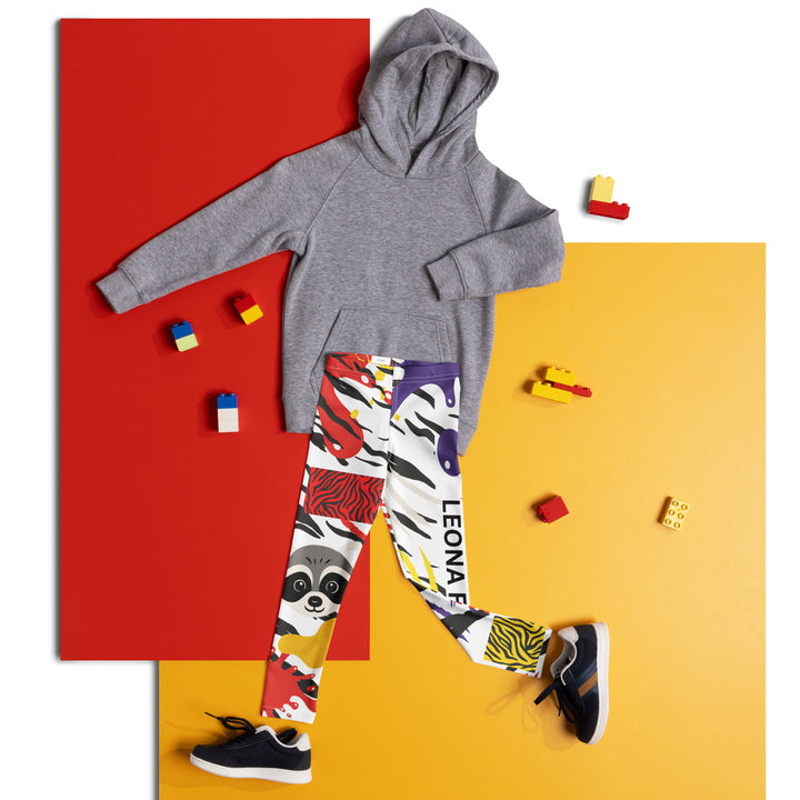  Raccoon Bandit Glow Girls Leggings, white base with splash-like spots in red, purple, and yellow, gray raccoon head, and wavy black stripes, front view laid flat on floor-with a visible 'Leona Fashion' text on the design