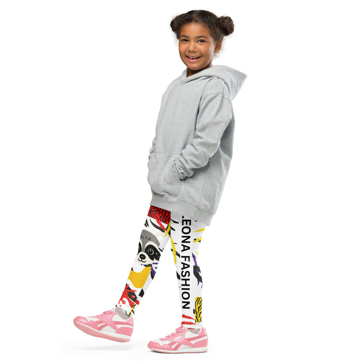 Raccoon Bandit Glow Girls Leggings, white base with splash-like spots in red, purple, and yellow, gray raccoon head, and wavy black stripes, front view with one leg lifted and extended on model-with a visible 'Leona Fashion' text on the design
