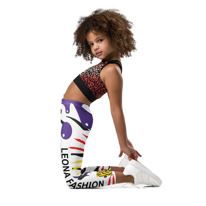  Raccoon Bandit Glow Girls Leggings, white base with splash-like spots in red, purple, and yellow, gray raccoon head, and wavy black stripes, left side view kneeling on model-with a visible 'Leona Fashion' text on the design