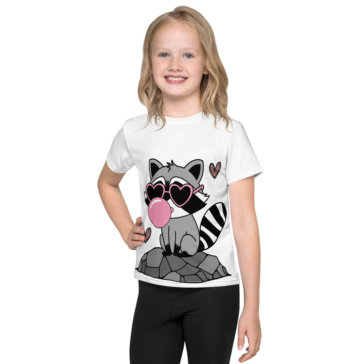 Raccoon Love Girls T-shirt – front view on model, white with gray raccoon standing on a rock blowing a pink bubble gum, wearing pink heart-shaped sunglasses, surrounded by pink tiger-striped hearts