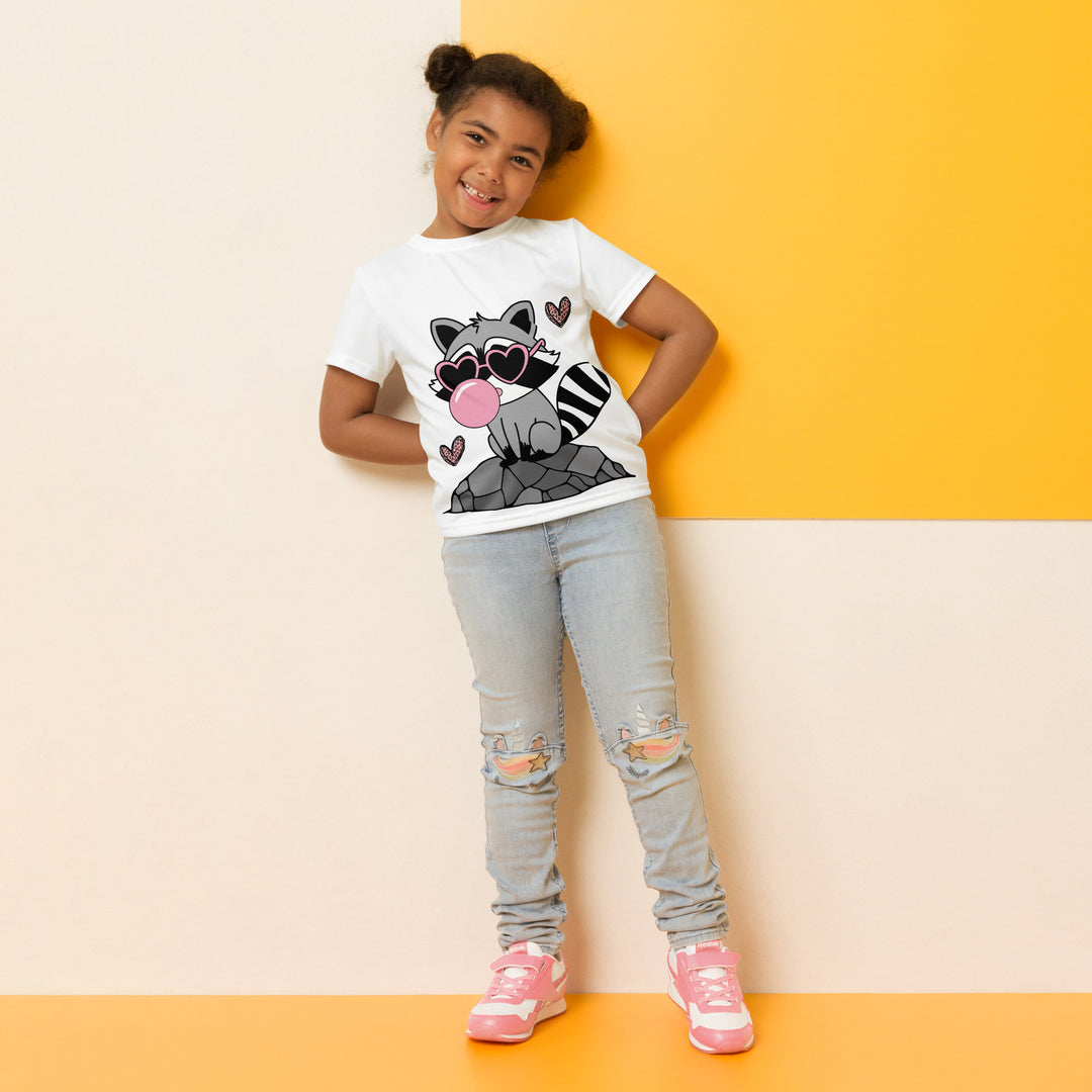 Raccoon Love Girls T-shirt – relaxed front pose on model, white with gray raccoon standing on a rock blowing a pink bubble gum, wearing pink heart-shaped sunglasses, surrounded by pink tiger-striped hearts