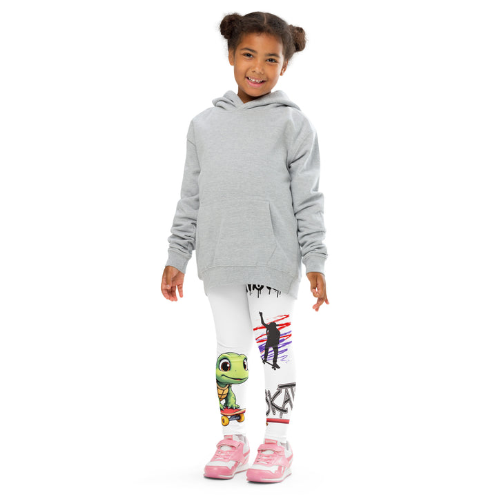 Skater Turtle Girls Leggings, white background with a green turtle riding a skateboard on one leg, black "MAKE YOUR MOVE" text and black skater silhouette with pink and purple motion lines on the other leg, and a skateboard with "skate" text at the bottom of the leg, front pose with arms at sides on model