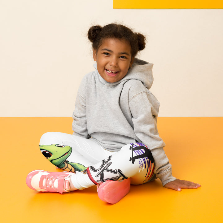 Skater Turtle Girls Leggings, white background with a green turtle riding a skateboard on one leg, black "MAKE YOUR MOVE" text and black skater silhouette with pink and purple motion lines on the other leg, and a skateboard with "skate" text at the bottom of the leg, seated pose on model