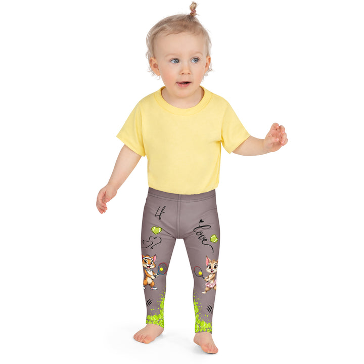 Tennis Kittens Girls Leggings, dark gray background with a cat holding a tennis racket on one leg and a kitten with a tennis racket on the other leg, each racket with a tennis ball as if playing, dressed in sporty outfits, with neon green tennis balls, hearts, and "love" text, front close-up view on model