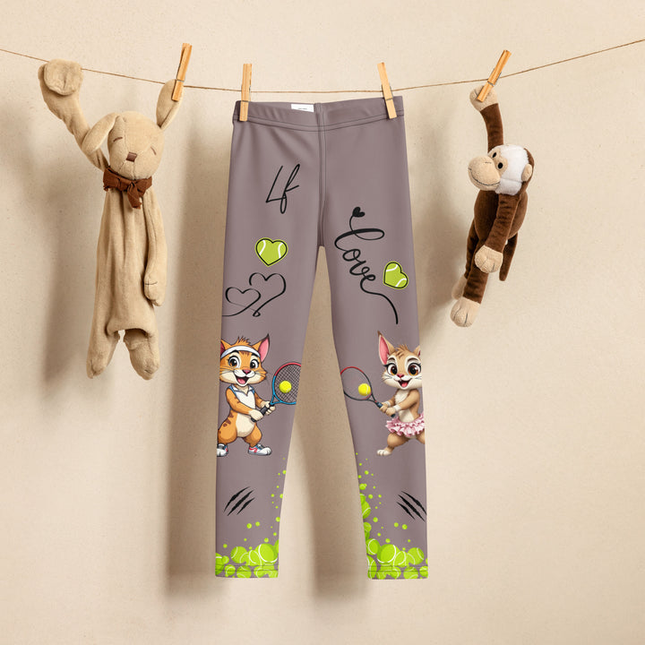 Tennis Kittens Girls Leggings, dark gray background with a cat holding a tennis racket on one leg and a kitten with a tennis racket on the other leg, each racket with a tennis ball as if playing, dressed in sporty outfits, with neon green tennis balls, hearts, and "love" text, front view on hanger