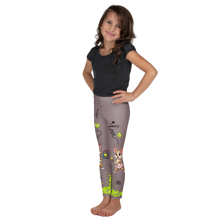 Tennis Kittens Girls Leggings, dark gray background with a cat holding a tennis racket on one leg and a kitten with a tennis racket on the other leg, each racket with a tennis ball as if playing, dressed in sporty outfits, with neon green tennis balls, hearts, and "love" text, left side view on model