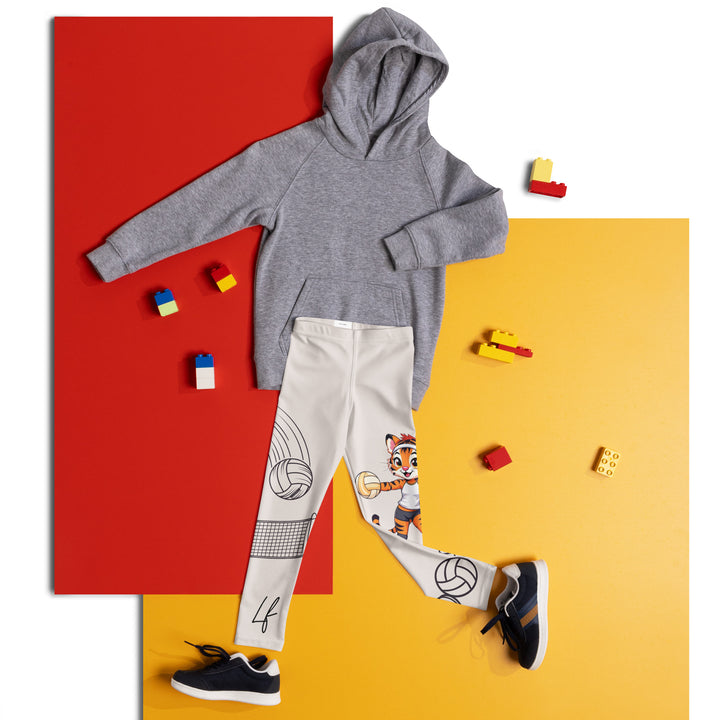 Volley Queen Tiger Girls Leggings, beige background with one leg featuring a sporty dressed tiger holding a volleyball, and the other leg with a volleyball net and a ball leaving a motion trail, front view laid flat on floor