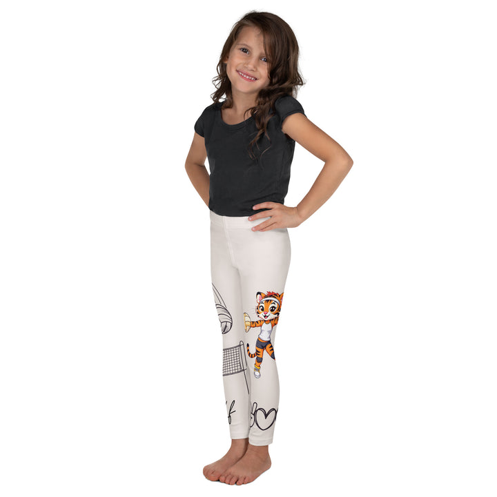 Volley Queen Tiger Girls Leggings, beige background with one leg featuring a sporty dressed tiger holding a volleyball, and the other leg with a volleyball net and a ball leaving a motion trail, left side view on model