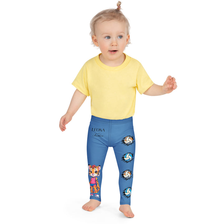 Volleyball Tiger Girls Leggings, blue background with a sporty dressed tiger holding a volleyball on one leg, and colorful glowing volleyballs on the other leg, front close-up view on model-with a visible 'Leona Fashion' text on the design