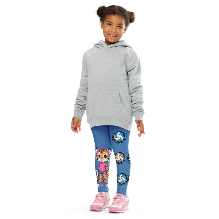 Volleyball Tiger Girls Leggings, blue background with a sporty dressed tiger holding a volleyball on one leg, and colorful glowing volleyballs on the other leg, front pose with arms at sides on model