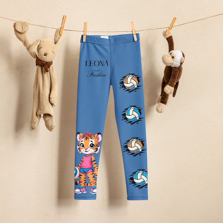 Volleyball Tiger Girls Leggings, blue background with a sporty dressed tiger holding a volleyball on one leg, and colorful glowing volleyballs on the other leg, front view on hanger-with a visible 'Leona Fashion' text on the design