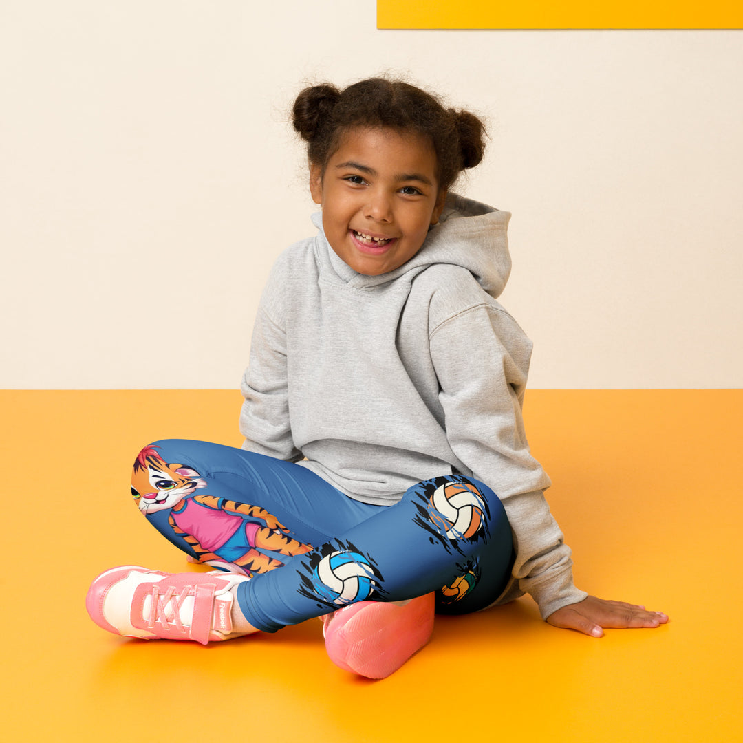 Volleyball Tiger Girls Leggings, blue background with a sporty dressed tiger holding a volleyball on one leg, and colorful glowing volleyballs on the other leg, seated pose on model