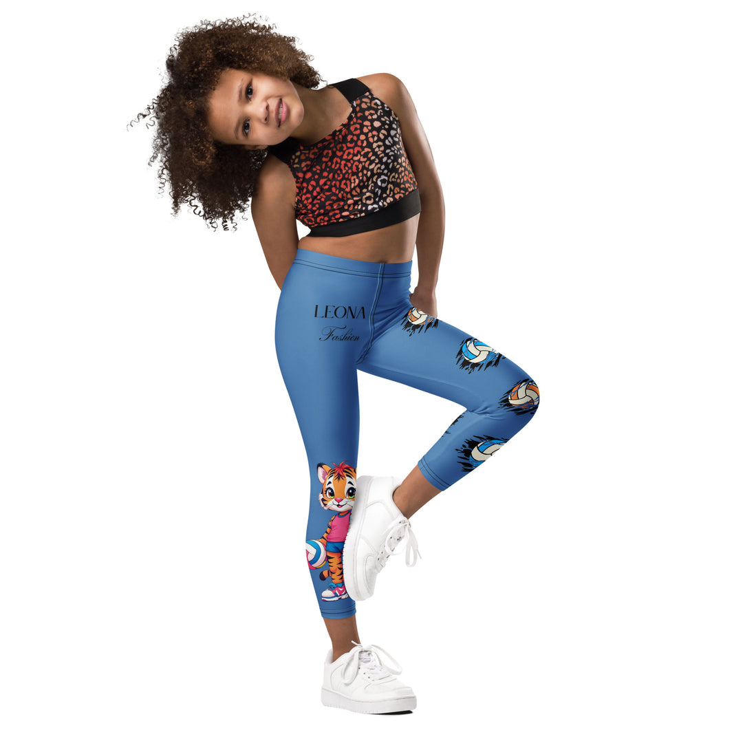 Volleyball Tiger Girls Leggings, blue background with a sporty dressed tiger holding a volleyball on one leg, and colorful glowing volleyballs on the other leg, side view with one leg lifted and bent on model-with a visible 'Leona Fashion' text on the design