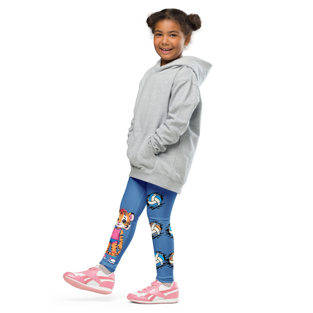 Volleyball Tiger Girls Leggings, blue background with a sporty dressed tiger holding a volleyball on one leg, and colorful glowing volleyballs on the other leg, side view with one leg lifted and extended on model