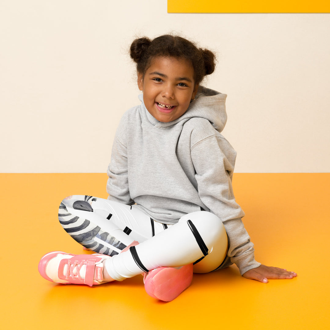 Model sitting – front view of Zebra Blush Glow Girls Leggings, white with black and white zebra print and blush pink stripes