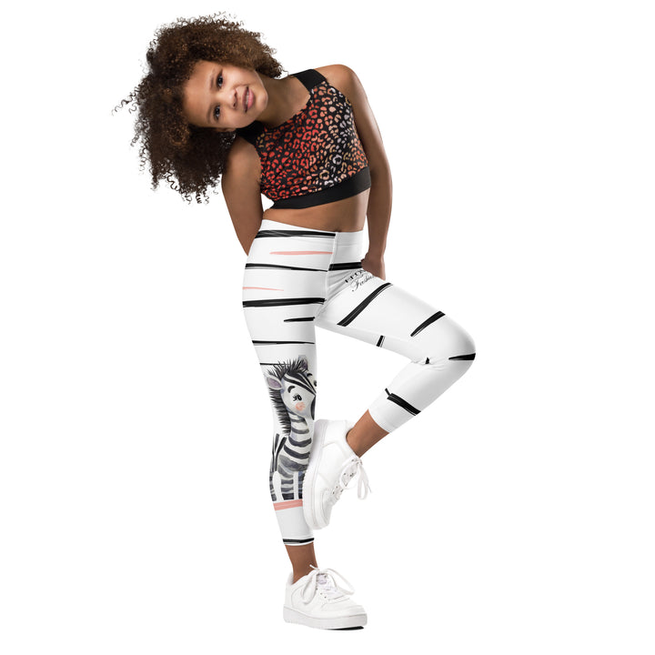Zebra Blush Glow Girls Leggings, white with black and white zebra print and blush pink stripes – side angle on model, one leg straight, other raised-with a visible 'Leona Fashion' text on the design